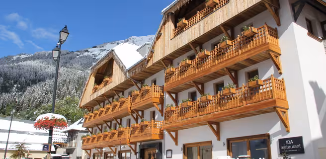 Bâtiment blanc avec balcons en bois, sol et sapins enneigés